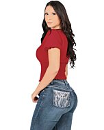 A woman wearing dark blue boot cut jeans with detailed white dreamcatcher embroidery on the back pockets, paired with a red short-sleeve top.
